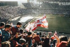 Vibrant crowd with flags cheering at a football stadium during the day.