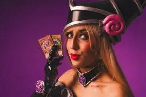 Cosplay of anime character Dark Magician Girl holding cards against a purple backdrop.